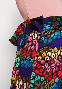 Jupe à imprimé léopard coloré avec des teintes vives de rouge, bleu, rose et vert sur un fond noir, avec un détail de noeud noué à la taille.