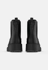 Czarne botki za kostkę o eleganckim designie, wykonane z gładkiego materiału; z masywną podeszwą i płaskimi uchwytami z tyłu.
