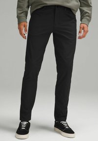 Kerged mustad slim-fit püksid on valmistatud kerge koega, millel on sile tekstuur ja standardtaskud, koos mustade tossudega ja valgete paeladega.