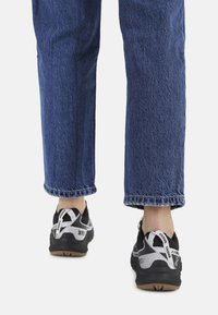 Baskets noires avec des accents blancs, présentant un design en maille texturée et une semelle flexible, assorties à un jean en denim bleu coupé aux chevilles.