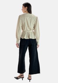Blusa beige con maniche a sbuffo e orlo peplum, stretta in vita. Abbinata a pantaloni neri a gamba larga e sandali con tacco.