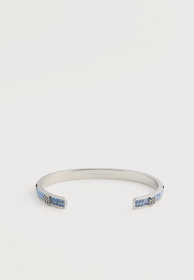 Ασημένιο μεταλλικό βραχιόλι με μπλε πολύτιμους λίθους και λογότυπα Tory Burch σε κάθε ανοιχτό άκρο, σε λευκό φόντο.