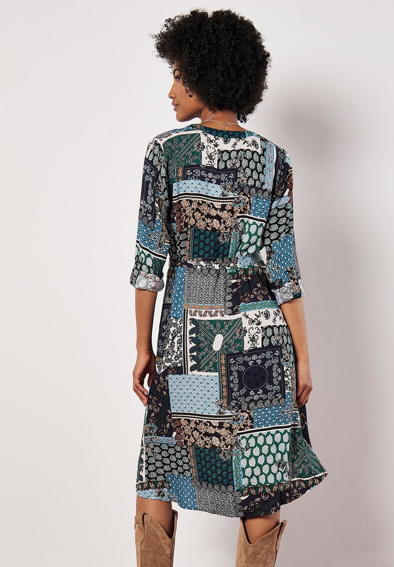 Pestré šaty s patchworkovým vzorem v zelené, modré a černé barvě. Dlouhé rukávy, přiléhavý pas a volný lem. Měkká textilie.