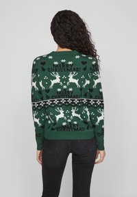 Grüner gestrickter Weihnachtspullover mit weißen Rentieren, Schneeflocken und dem Text "FROHE WEIHNACHTEN!" in Schwarz. Klassische Passform mit geripptem Saum.