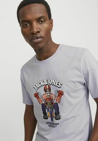 Lyse lilla t-shirt med korte ærmer, der har et farverigt grafisk motiv af et skelet, der kører på en motorcykel, med teksten "Jack & Jones" og "Worldwide Originals".