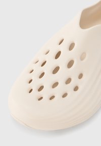 Ελαφριά μπεζ παπούτσια με ομαλή, υφασμάτινη επιφάνεια που διαθέτει πολλαπλές οβάλ οπές για αερισμό και στρογγυλεμένη σχεδίαση μύτης.