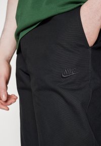 Svarta Nike-byxor i stretchmaterial, med en broderad logotyp på framsidan och en slät textur samt en slim fit-design.