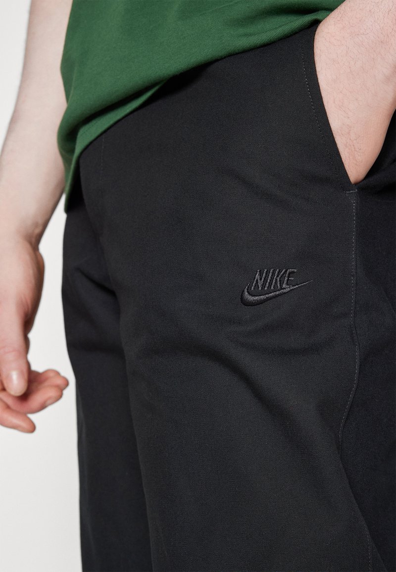 Pantalon Nike noir en tissu extensible, avec un logo brodé à l'avant et une texture lisse au design ajusté.