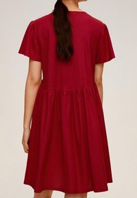 Abito rosso a ginocchio realizzato in tessuto morbido. Maniche corte, vita arricciata e gonna ampia. Presenta un collo tondo e senza motivi visibili.