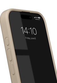 Beige telefondeksel rundt en svart smarttelefonskjerm som viser tid og dato. Sideknapper er synlige og teksturerte. 5G-indikator vist.