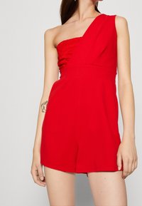 Mono rojo de un solo hombro con cuerpo texturizado, tejido suave y pantalones cortos ajustados. Presenta una cintura ceñida y líneas limpias.