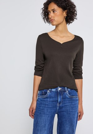 Haut long à manches brun foncé avec un décolleté en V et une seule fermeture à pression, associé à un jean en denim bleu à coupe classique avec poches.