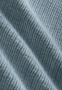 Struktureret stof i lyseblå med lodrette ribbede mønstre. Blød overflade med bølgende udseende, der fremhæver dybde og dimension.