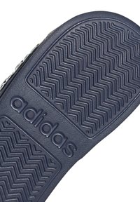 Podeszwa buta Adidas z granatowej teksturowanej gumy, z zygzakowymi wzorami bieżnika oraz wyraźnym wytłoczonym logo po boku.