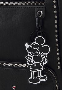 Schwarze Lederhandtasche mit silbernem Reißverschluss und Nieten. Mit einem schwarz-weißen Mickey Mouse Gummischlüsselanhänger, der mit einem Metallkarabiner befestigt ist.