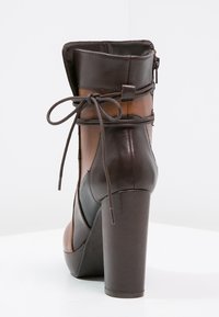 Bruine leren enkellaars met hoge hak, een rits aan de achterkant en een decoratieve veter die om het bovenste deel is gebonden.