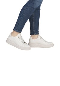 Weiße Leder-Sneaker mit einer dicken, strukturierten Sohle, laced-Up Design und dezenten seitlichen Akzenten. Getragen mit engen blauen Jeans.