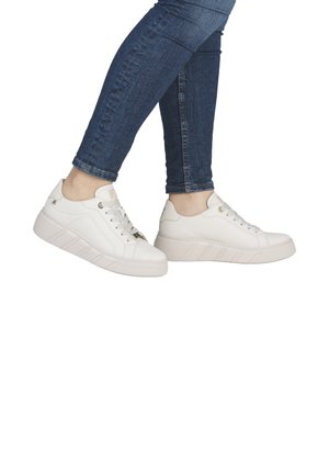 White leather sneakers with a thick, textured sole, featuring lace-up design and subtle side accents. Worn with fitted blue jeans.