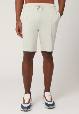 Shorts da ginnastica grigi chiari con vita con cordino, dotati di tasche laterali e un tessuto liscio e testurizzato. Abbinati a sneaker multicolori.