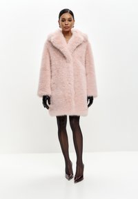 Rosa faux fur frakke med bred krave, lange ærmer og knaplukning. Båret med gennemsigtige sorte strømpebukser og spidse hæle.