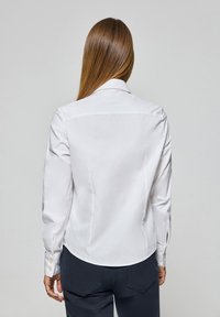 Witte lange mouwen shirt met een kraag, knoopmanchetten, een getailleerd ontwerp en een gladde textuur. Gedetailleerde stiksels langs de achterkant.