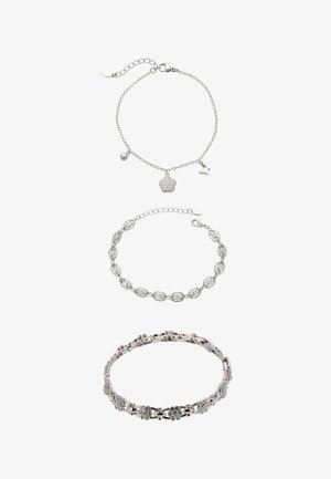 Drei silberne Armbänder: Das oberste mit kleinen Anhängern, das mittlere in einem massiven Gliederdesign und das unterste mit floralen Mustern und Akzenten.