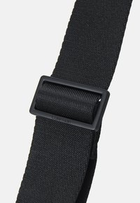 Sangle en tissu noir avec une texture lisse, dotée d'une boucle rectangulaire noire mate, présentant un logo Calvin Klein subtil.