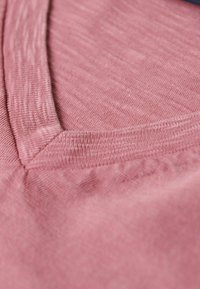 Rosa, texturerad tyg med v-ringning, som visar ett subtilt heather-mönster och ett mjukt, lätt material.