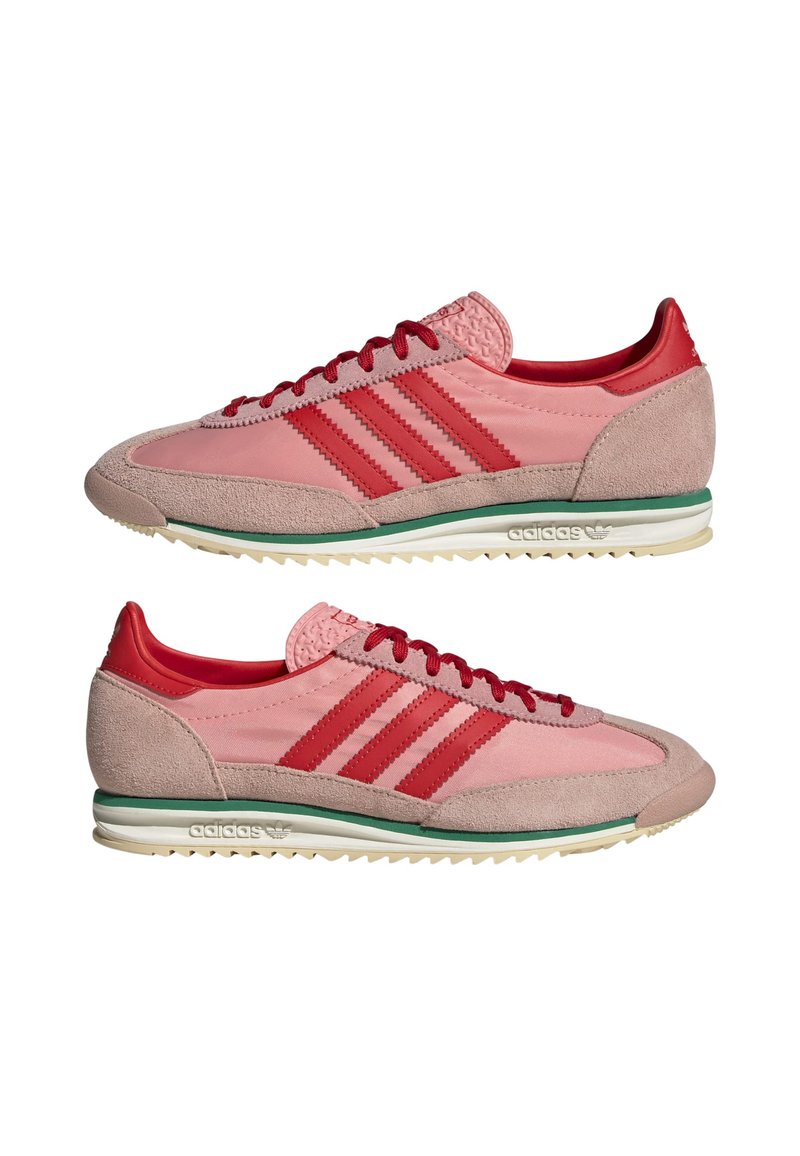 Baskets Adidas avec un mélange de matériaux rose clair et rouge, trois bandes rouges, des accents en suede et une semelle blanche bordée de vert.