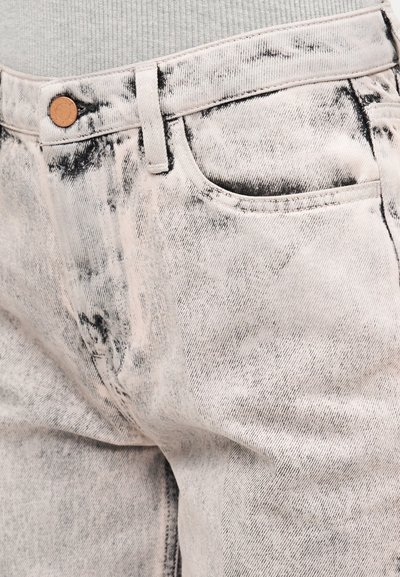 Κοντινό πλάνο ξεθωριασμένου μονόχρωμου γκρι τζιν με μαύρες λεπτομέρειες πλύσης και χάλκινο κουμπί, φορεμένο πάνω από γκρι ριμπ ύφασμα κορυφή.