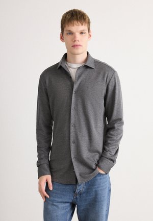Camicia grigia a maniche lunghe con colletto button-down, realizzata in tessuto morbido, caratterizzata da un taglio dritto e una trama sottile, abbinata a jeans blu.