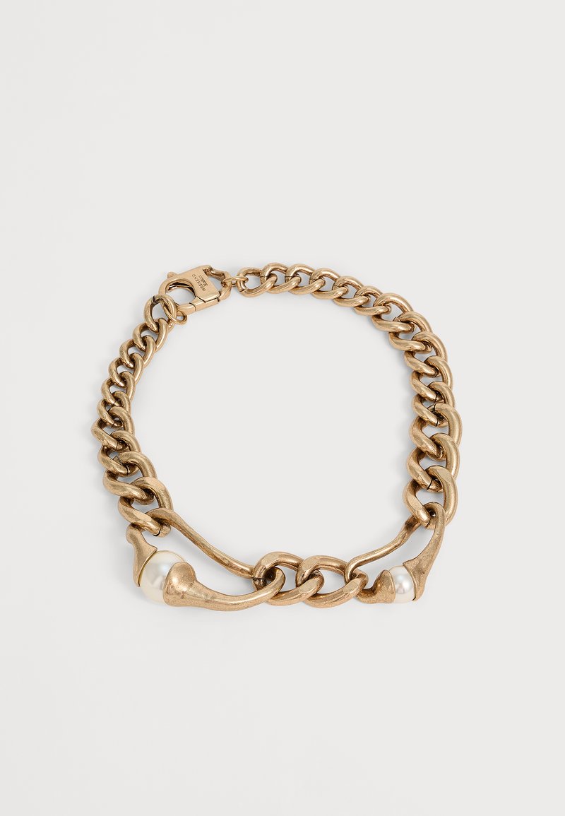 Bracelet chaîne en or épais avec des maillons courbes et deux accents de perles blanches sur un fond clair.