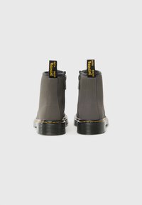 Botins cinzentos até ao tornozelo com material de borracha suave, fechos de correr laterais e alças amarelas em contraste. Apresentam uma sola grossa e texturizada com costura amarela.