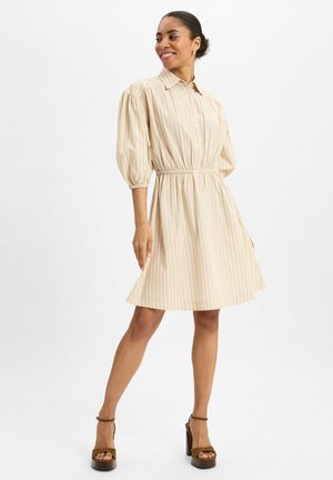 Beige gestreepte jurk met korte pofmouwen, een getailleerde taille en een uitlopende rok. Gecombineerd met bruin met hakken.