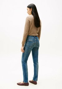 Suéter marrón claro, jeans de mezclilla azules y bailarinas moradas. Jeans ajustados con bolsillos traseros y detalles de costura visibles.