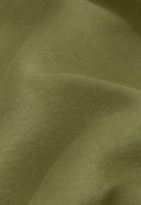 Gros plan d’un tissu lisse vert olive avec une texture fine en maille visible et des plis doux.