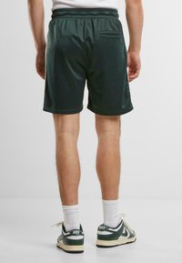 Shorts de sport verts en tissu lisse, avec une taille élastique et une poche arrière unique. Les shorts ont une longueur jusqu'aux genoux et des coutures discrètes.