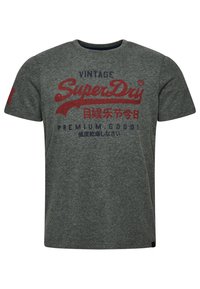 T-shirt en coton gris à manches courtes, arborant le logo et le texte "SuperDry" en rouge et bleu. Encolure ronde et texture douce.