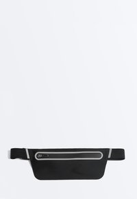 Sac banane noir et fin avec une poche zippée et une sangle réglable, comportant des bandes réfléchissantes le long de la fermeture éclair et aux extrémités de la sangle.