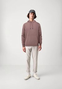 Hanorac cu glugă în culoarea roz prăfuit, cu buzunar frontal și șnururi, asortat cu pantaloni bej deschis și adidași albi.