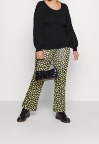 Top nero a maniche lunghe con spalle arricciate, abbinato a pantaloni larghi gialli con motivo floreale. Accessoriato con una borsa a tracolla nera trapuntata.
