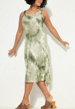 Vestido sin mangas de tie-dye verde con corte relajado, abertura lateral y tejido suave. Llevado con zuecos de plataforma marrones.