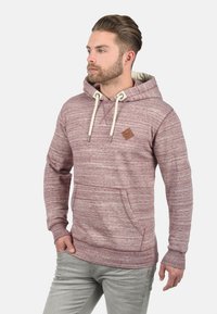 Bordowa bluza z kapturem o strukturalnej tkaninie, z przednią kieszenią, sznurkiem ściągającym oraz małą brązową skórzaną naszywką z logo na piersi.