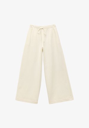 Pantalons larges crème avec taille élastique et cordon de serrage. Texture lisse, mi-genoux, avec une coupe ample et sans motifs visibles.