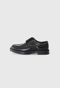 Black leather lace-up shoes with decorative studs along the seams, rounded toe, and a thick, flat black rubber sole.