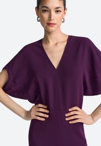 Paarse jurk met korte, brede mouwen en een diepe V-hals. Glad, gestructureerd stof met een getailleerde pasvorm en subtiele naaddetails.