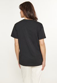 Sort T-shirt med korte ærmer og afslappet pasform, lavet af blødt bomuldsstof. Bagudsigt viser en lige kant.