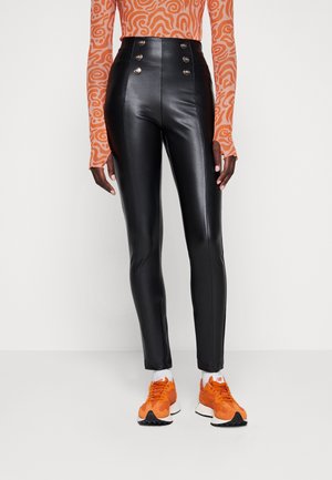 Person wearing high-waisted black faux leather pants with silver buttons, patterned orange long-sleeve top, white socks, and orange sneakers.