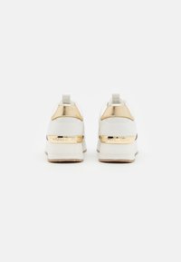 Witte sneakers met een metallic gouden hiel en logo-accent. Voorzien van een gladde textuur en een verhoogd, gestructureerd zoolontwerp.