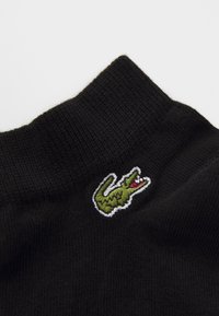 Chaussette noire côtelée avec un logo de crocodile vert brodé, présentant des accents rouges et une surface texturée.